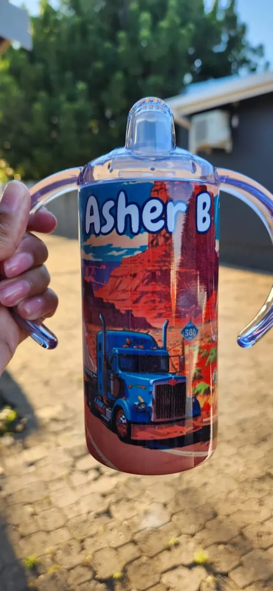 Kids sippy cup with two handles printed with a blue truck in a desert canyon and the name Asher B