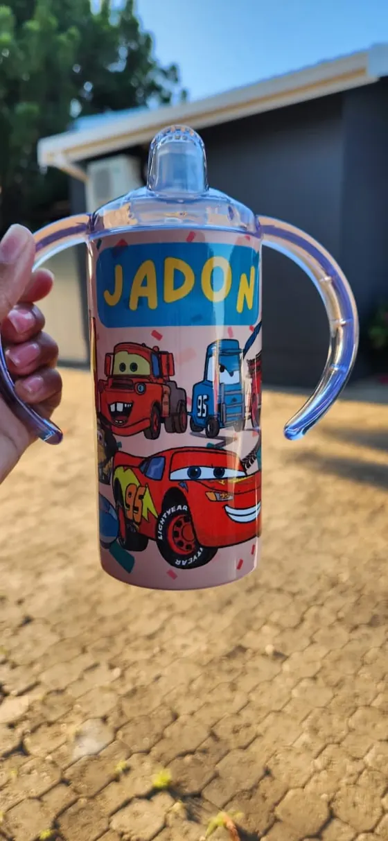 Kids sippy cup with two handles printed with cartoon racing cars and the name JADON on pink